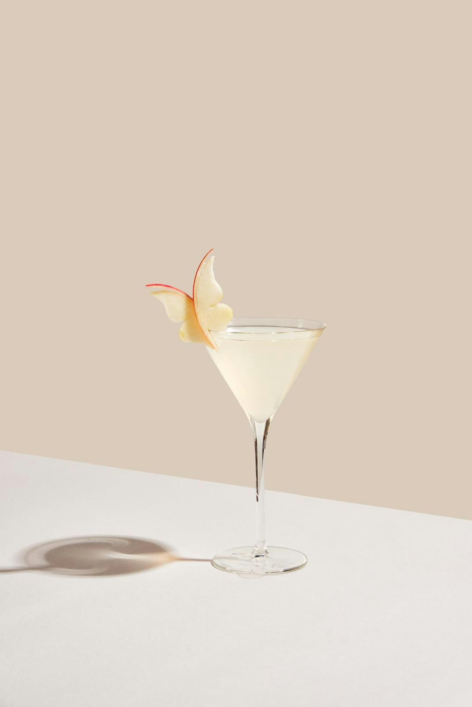 A clear citrus martini with apple-flower garnish
